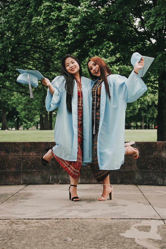 Two women celebrating graduation in cap and gown, expressing happiness outdoors.